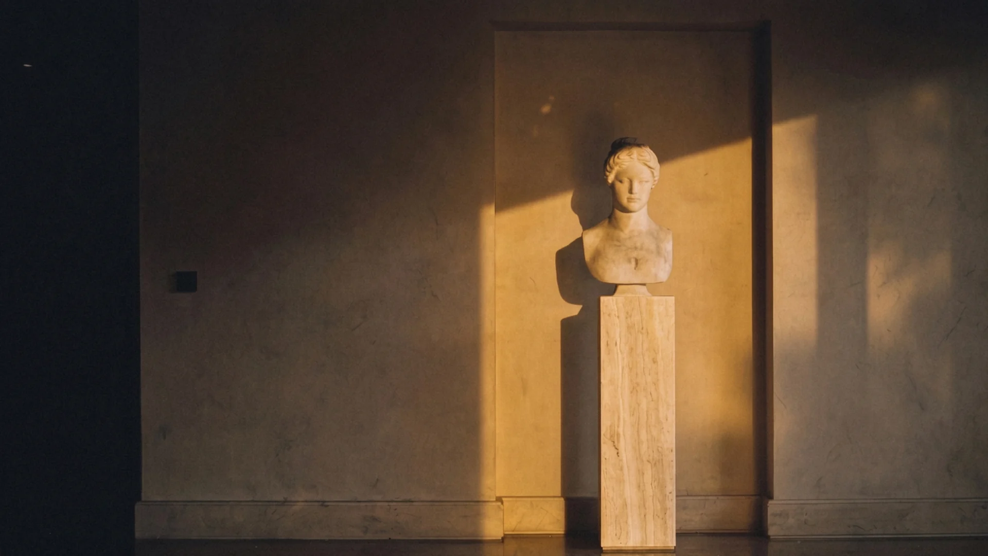 A classical marble bust on a travertine plinth in warm evening light.